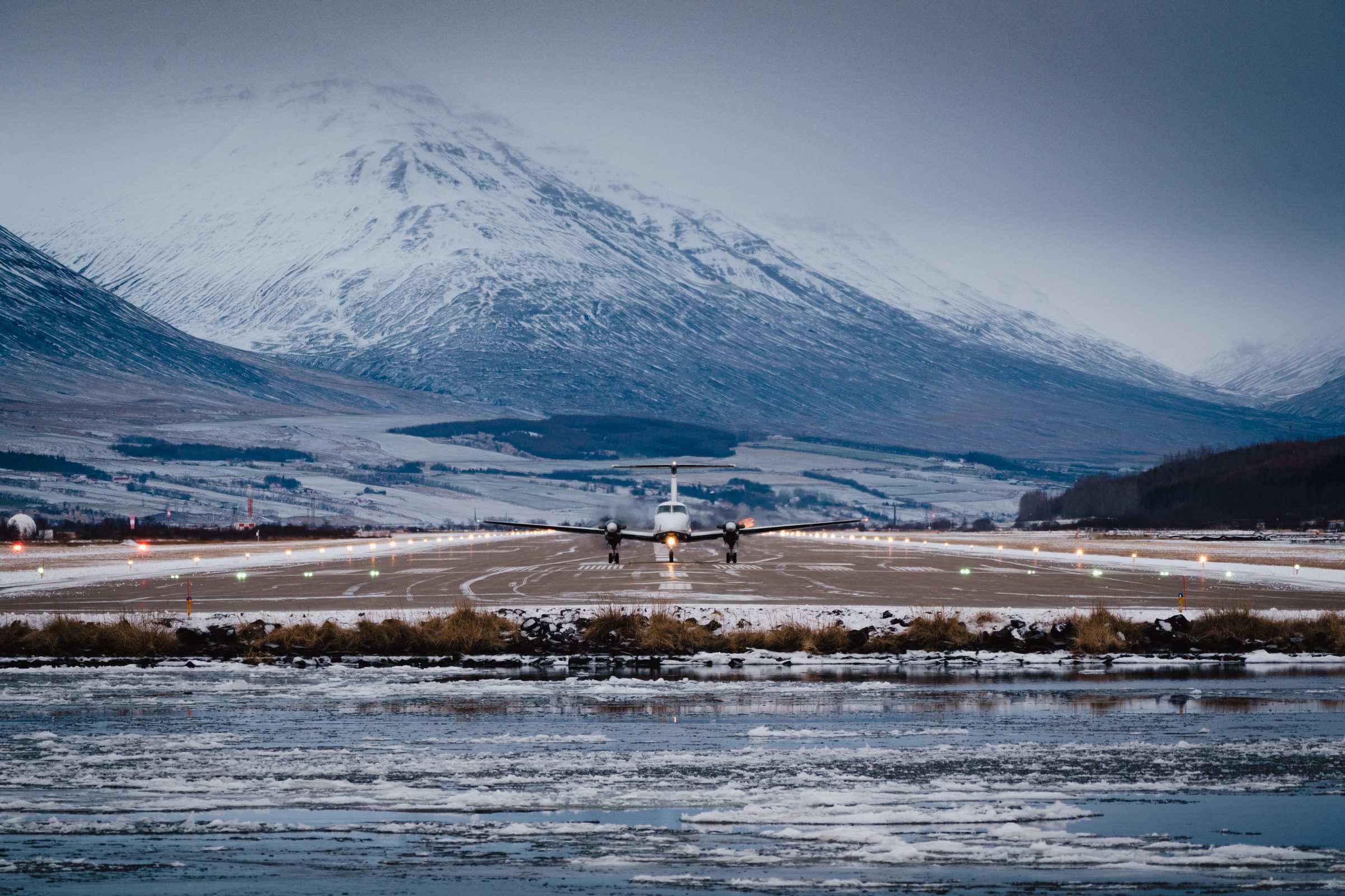 Small propeller plane on a runway with snow-covered mountains behind it