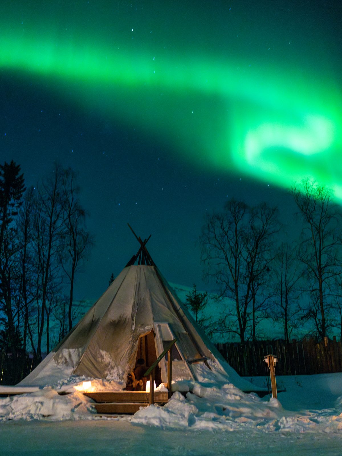 Campfire in front of a lavvu tent under the northern lights